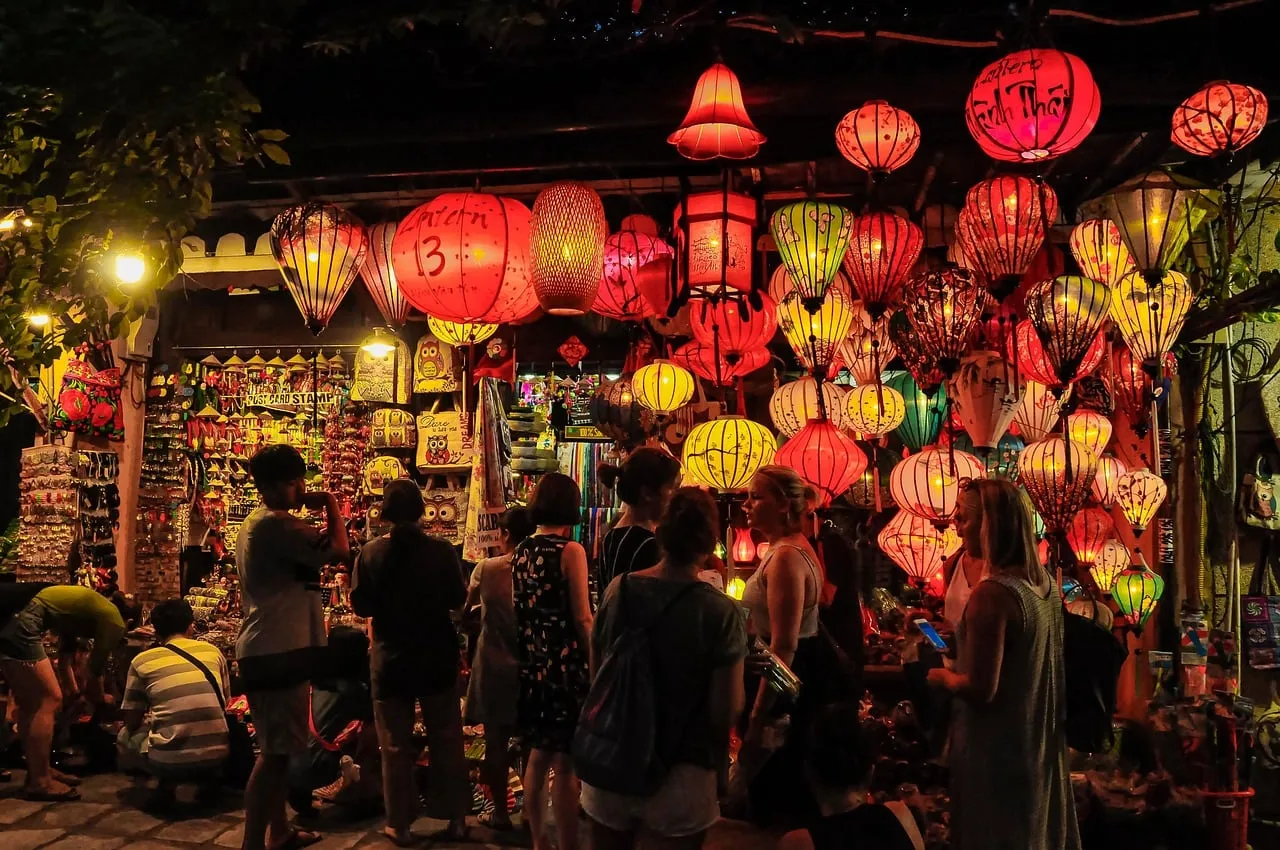 Di sera, un gruppo di persone davanti a un negozio di strada illuminato da molte lanterne colorate rosse, gialle e verdi.